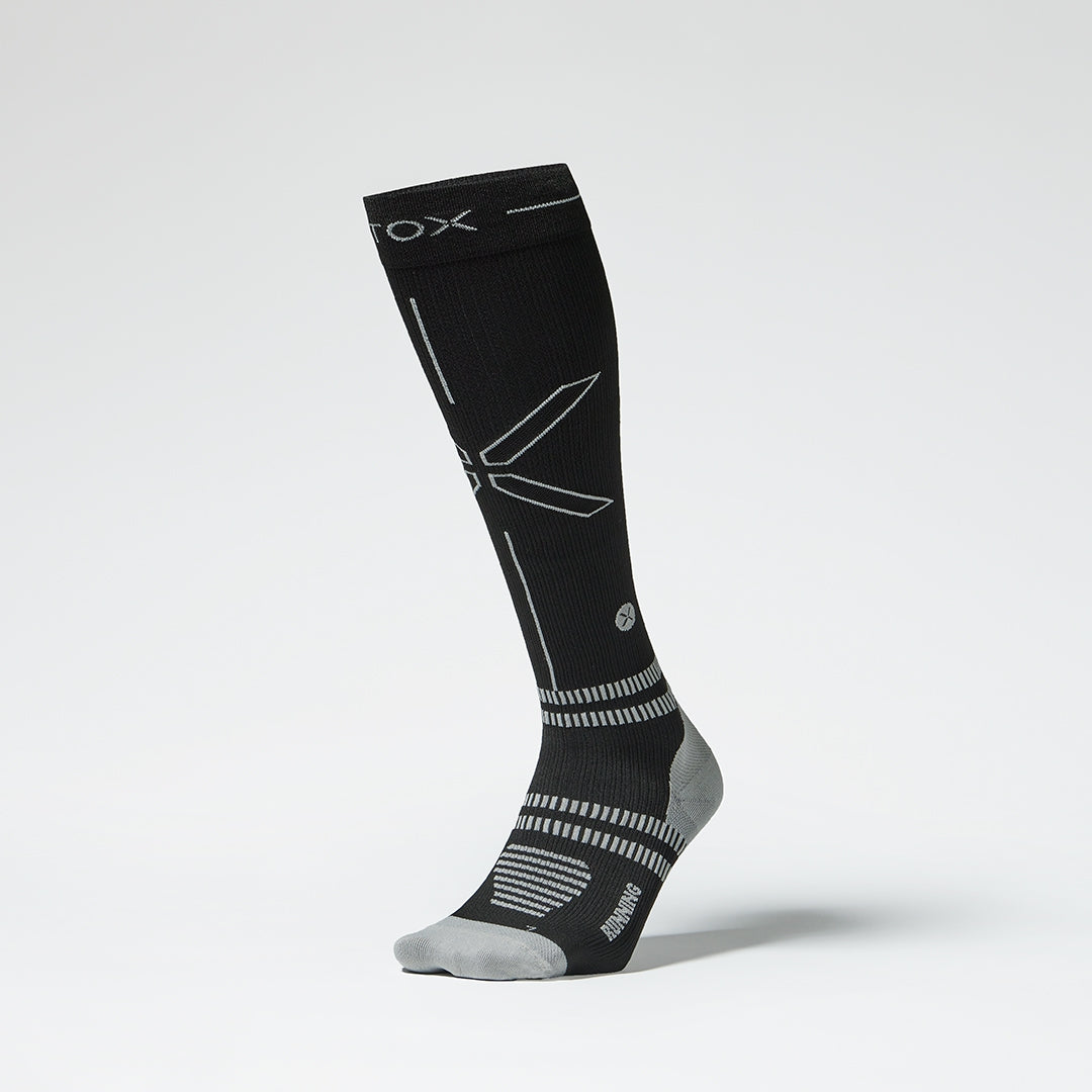 Front view of a black colored knee high compression sock with grey accents. 