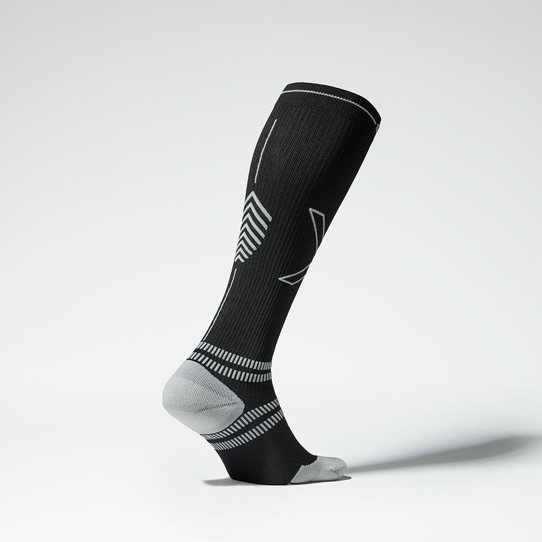 Side view of a black colored knee high compression sock with grey accents. 