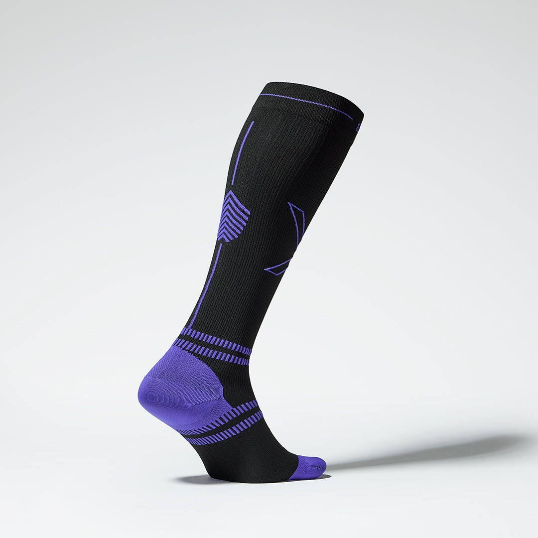 Side view of a black colored knee high compression sock with purple accents. 