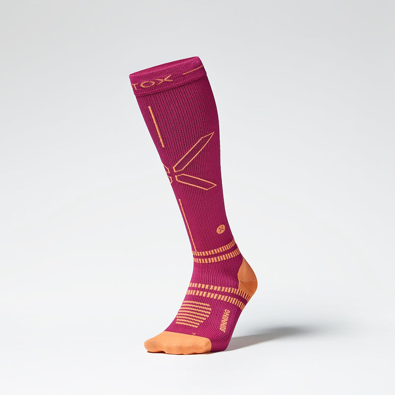 Front view of a fuchsia colored knee high compression sock with orange accents.