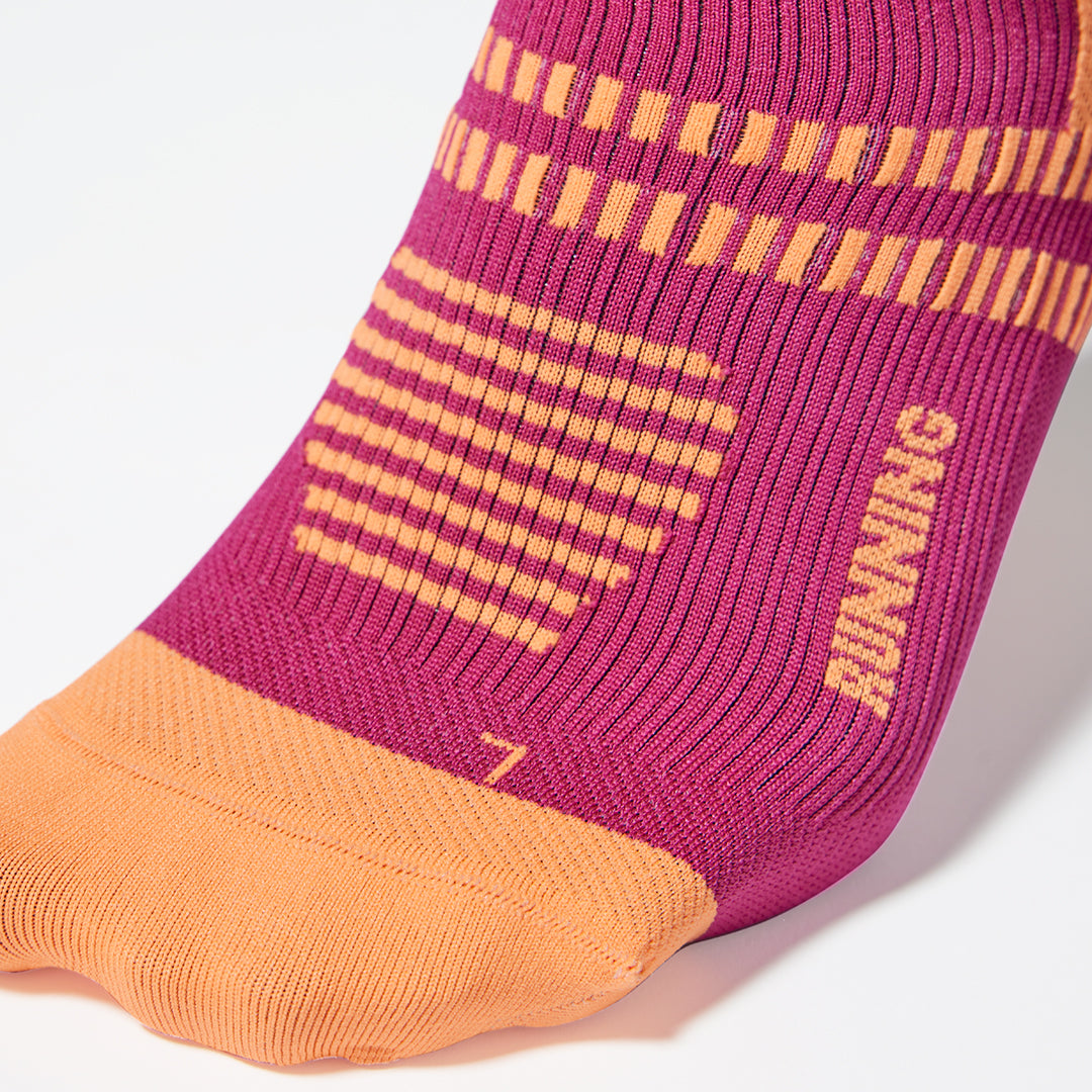 Close up of toes in a fuchsia colored compression sock with orange details.