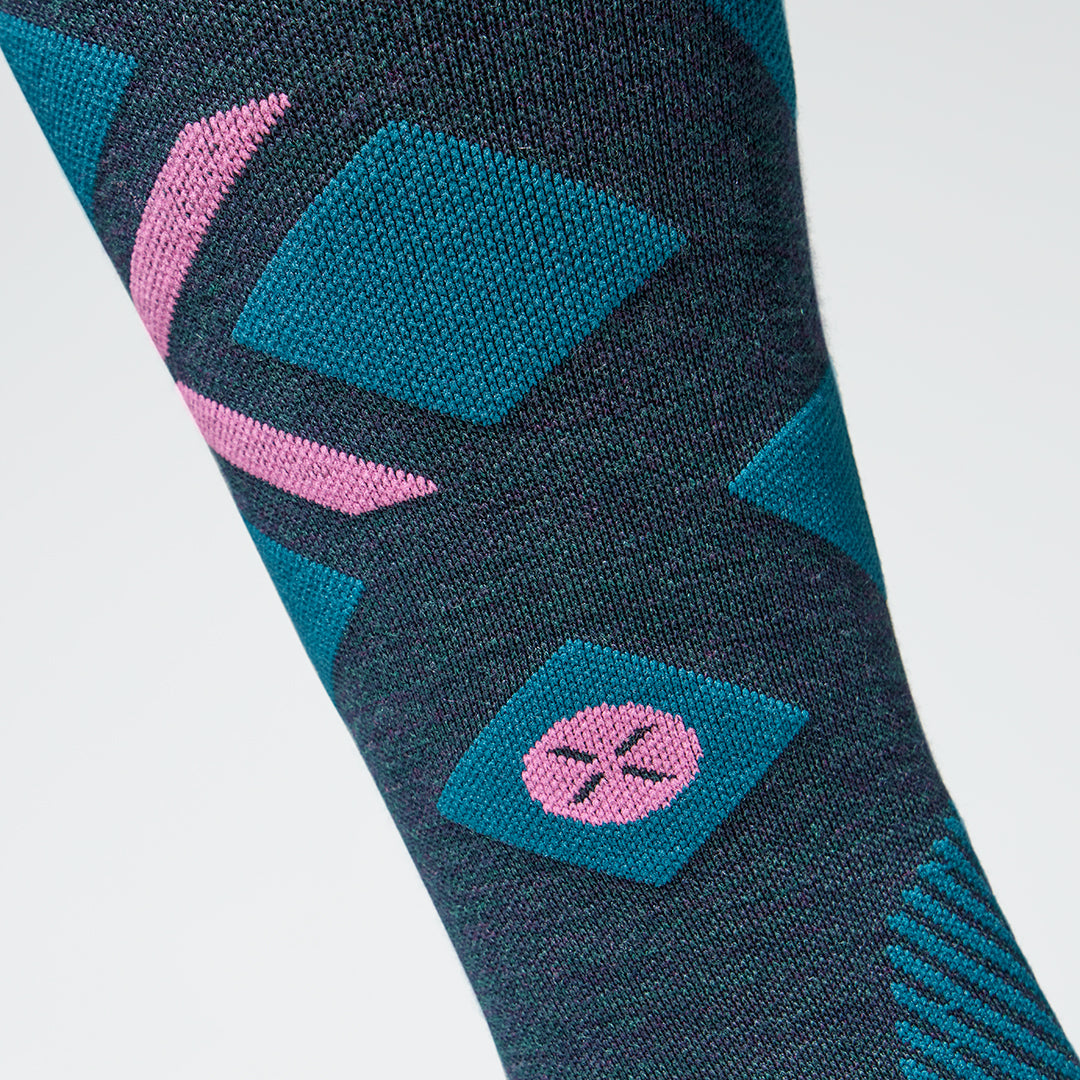 Close up of a teal high compression sock with a pink logo.