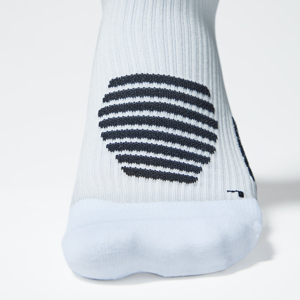 Close up of the front of a white compression sock with black accents. 