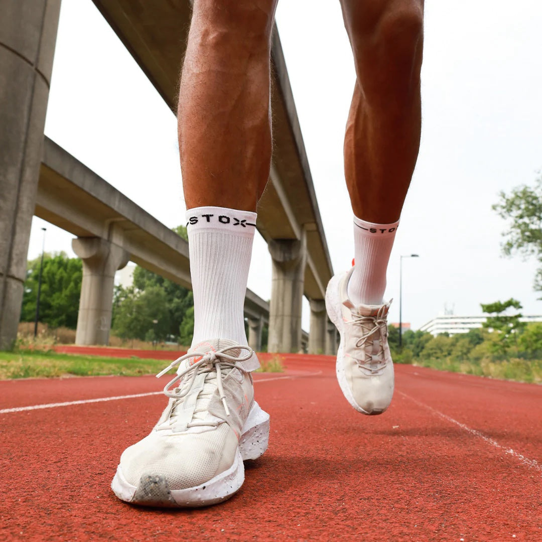 Legs of a man running on a track wearing white ankle high socks.