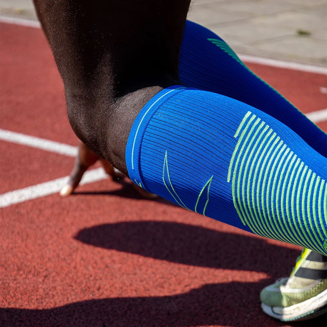 Man getting ready for a sprint wearing blue calf sleeves with green details. 