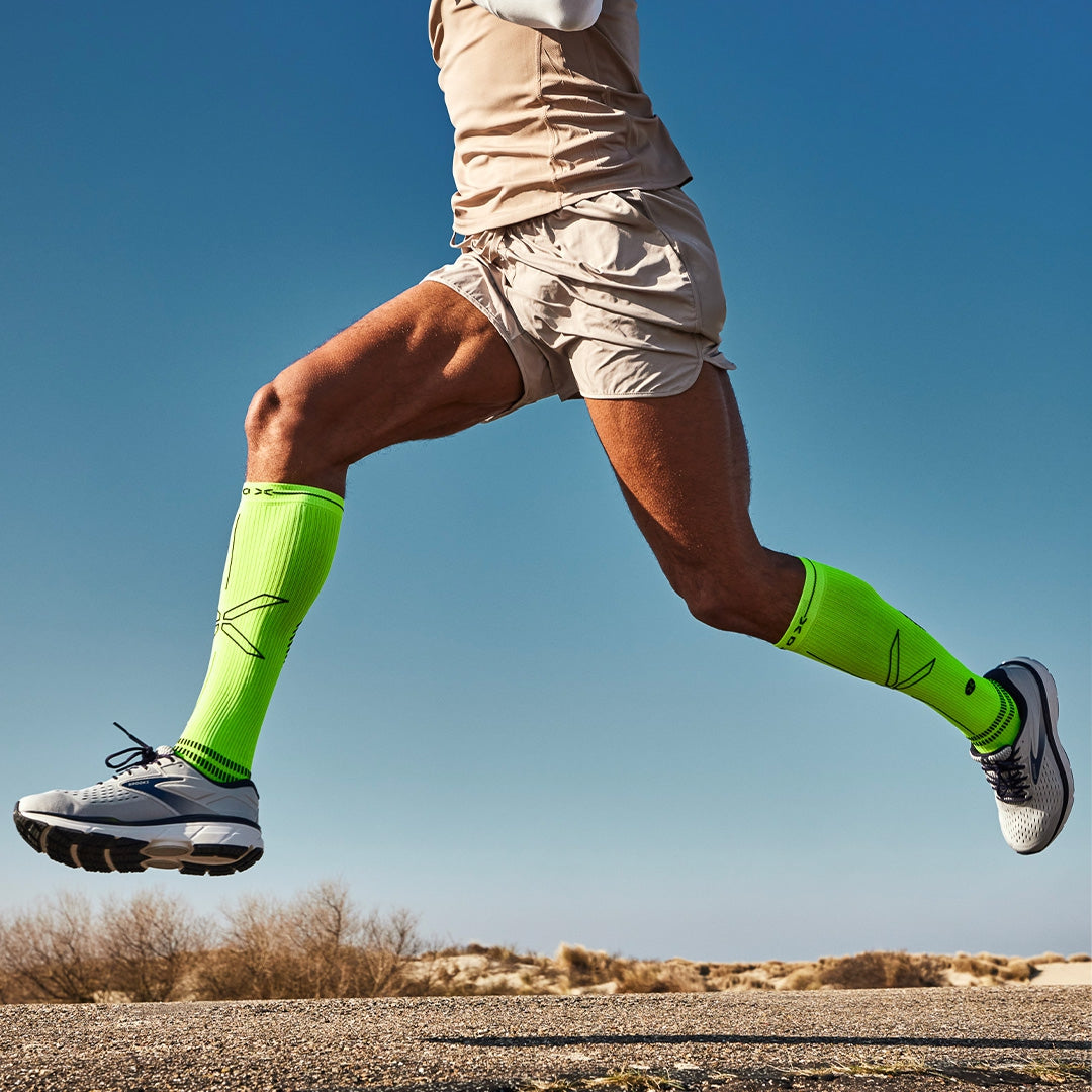 Man running in yellow socks with blue skies behind him. 