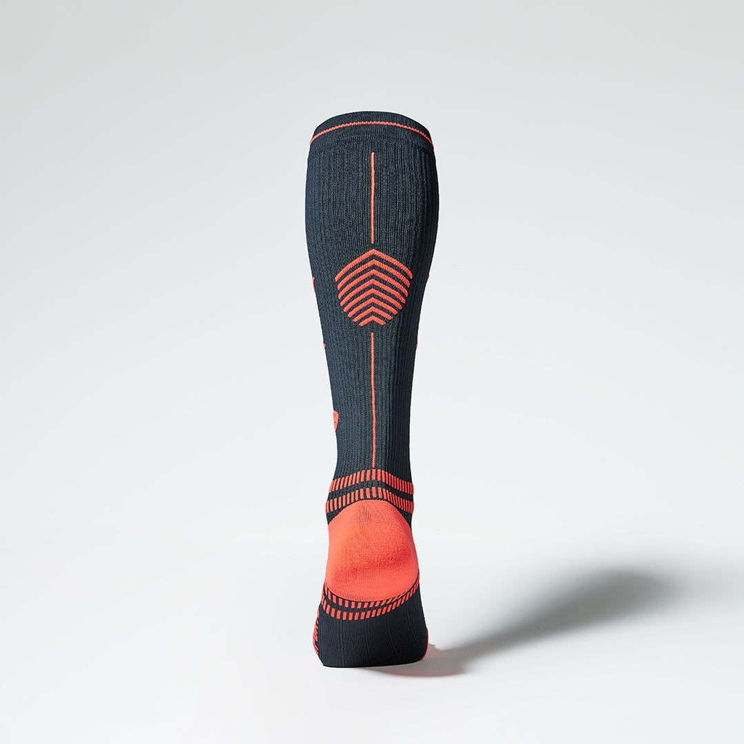 Back view of a knee high compression sock in navy blue with orange heel.