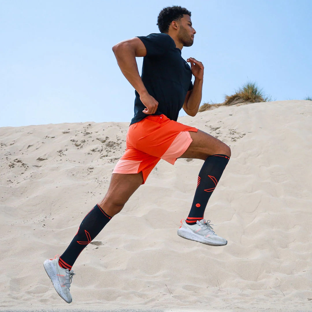 Man running across sand wearing orange shorts. 