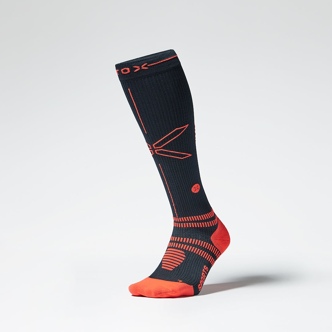 A knee high navy blue compression sock with orange details from the front.