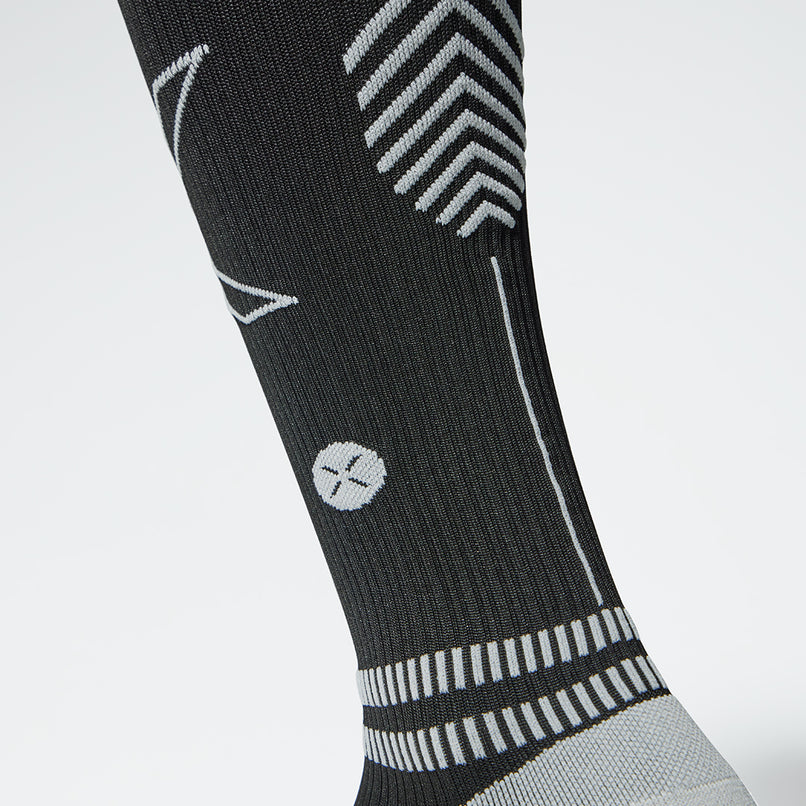 The front view of a knee high compression sock in black with grey details.