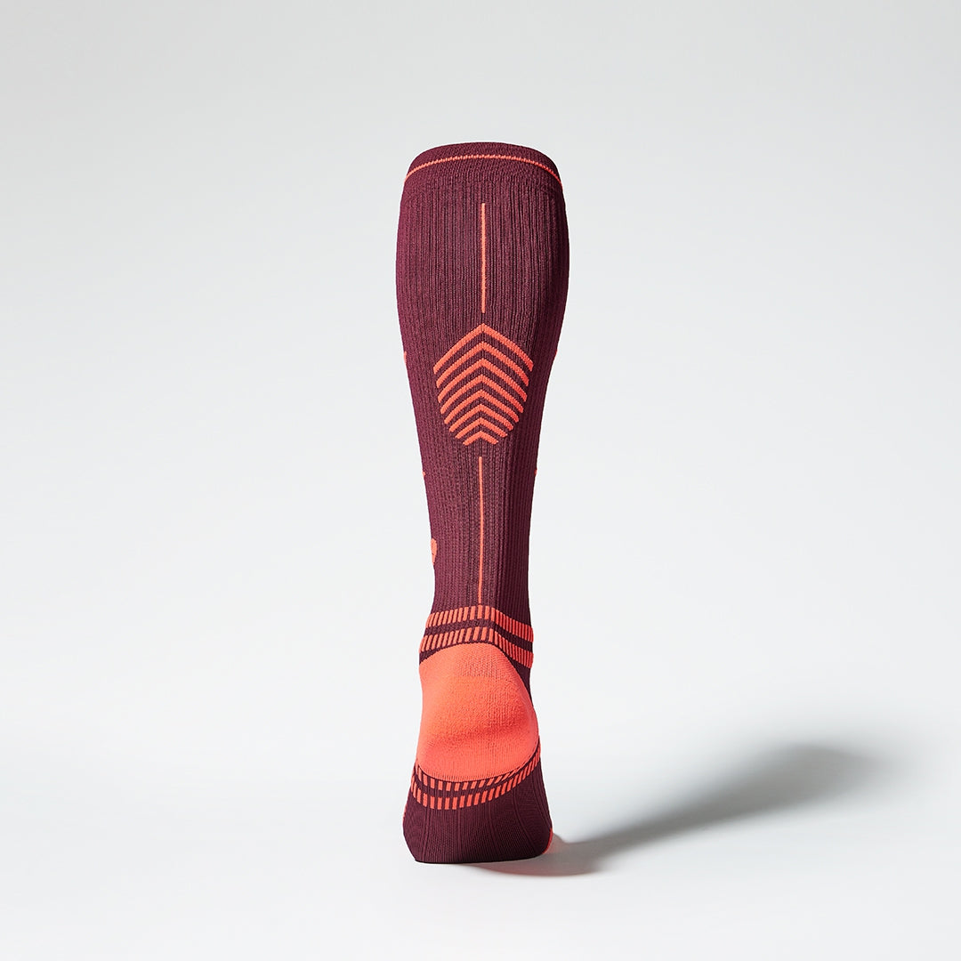 View of the back of a knee high compression sock in bordeaux with orange accents. 
