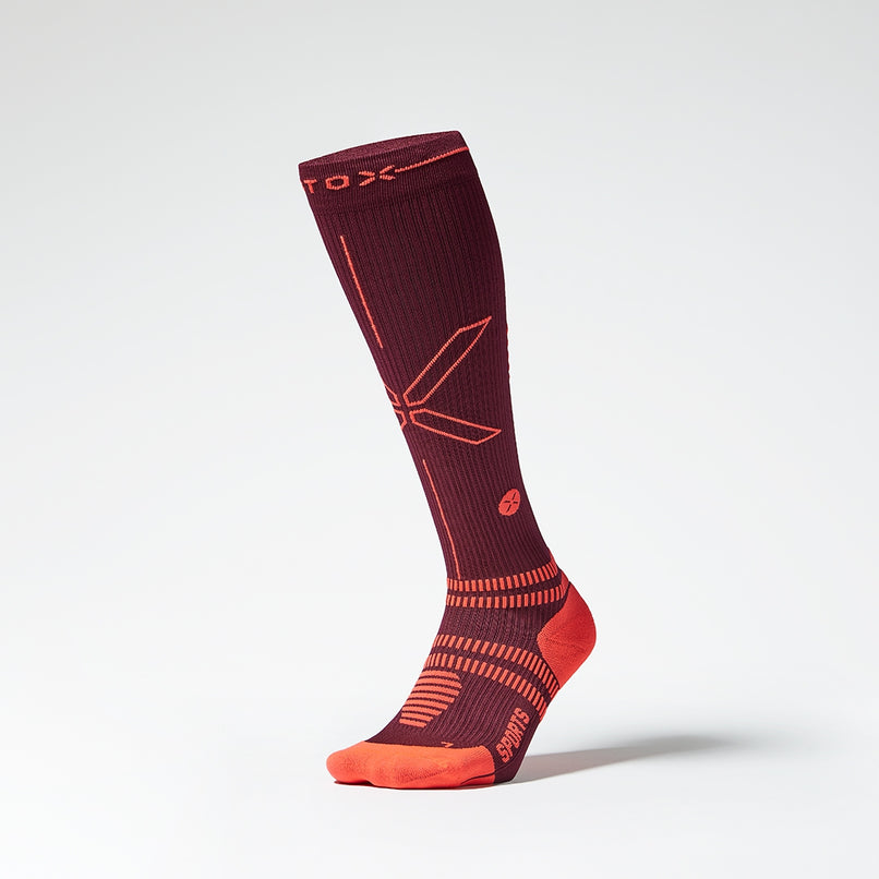 Front view of a knee high compression sock in bordeaux with orange accents. 