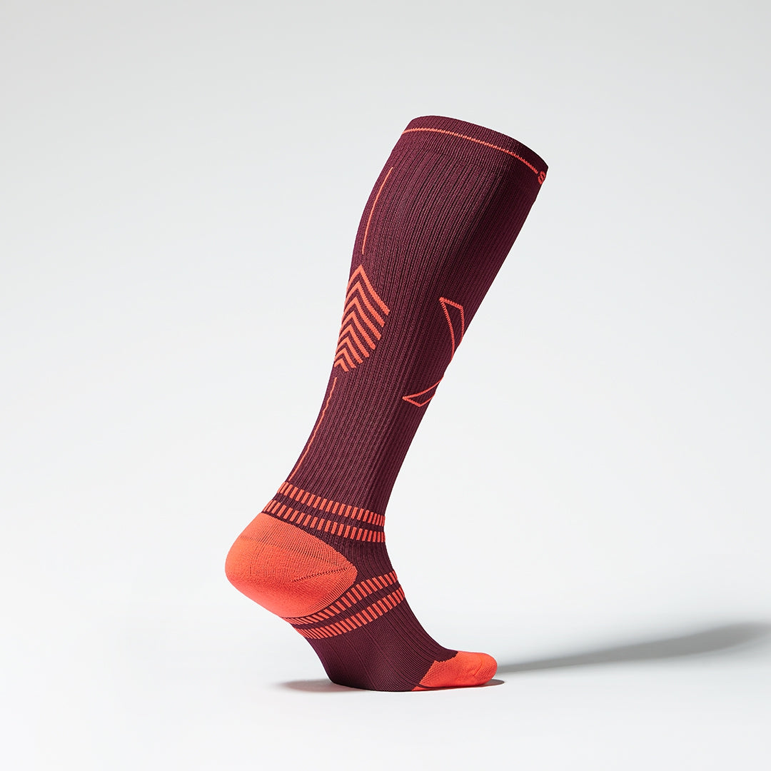 Side view of a bordeaux coloured knee high compression sock with orange accents. 