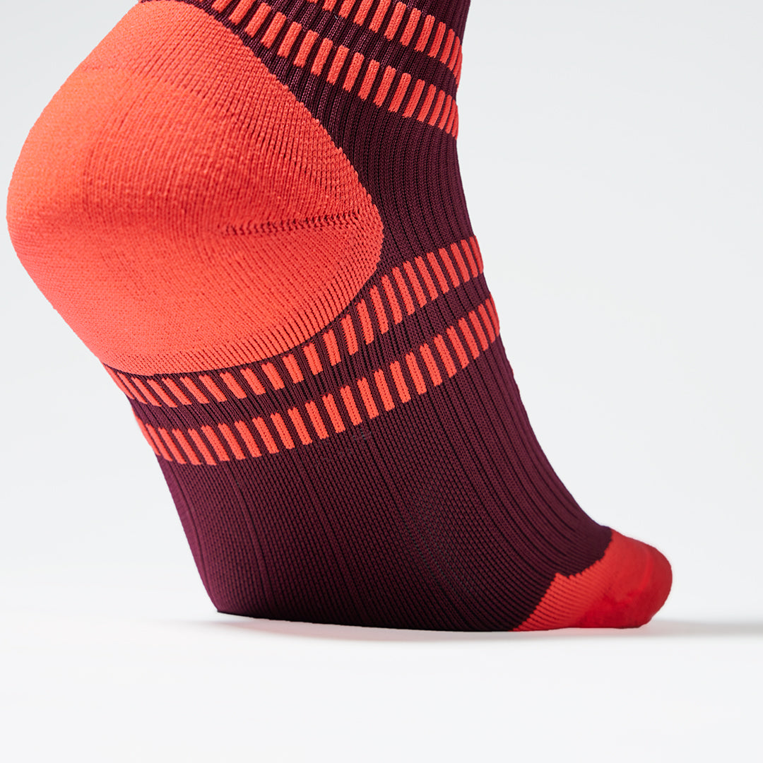 Close up of a bordeaux coloured compression sock with orange details. 