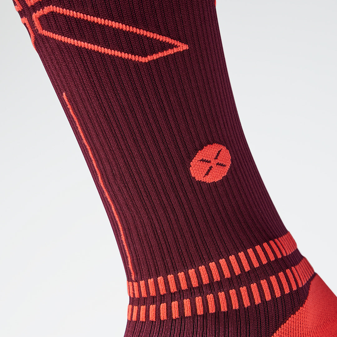 Close up of a bordeaux coloured compression sock with an orange coloured logo. 