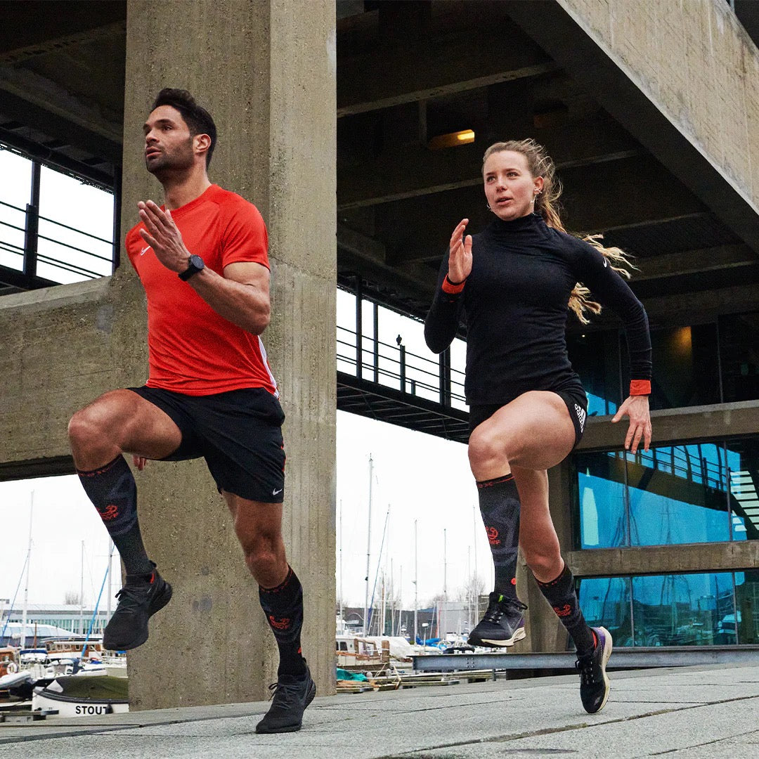 Two people running in black and red clothing with sail boats in the background.