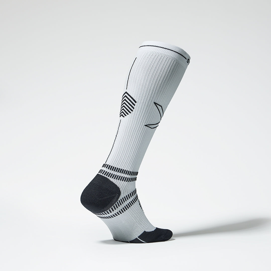 Side view of a white colored knee high compression sock with black details. 