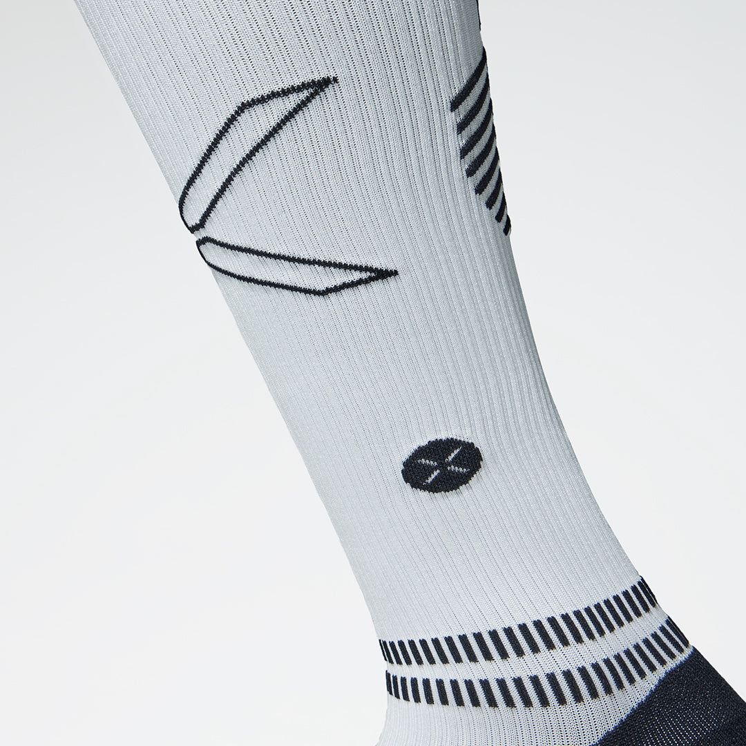 Close up of a white compression sock with a black coloured logo. 