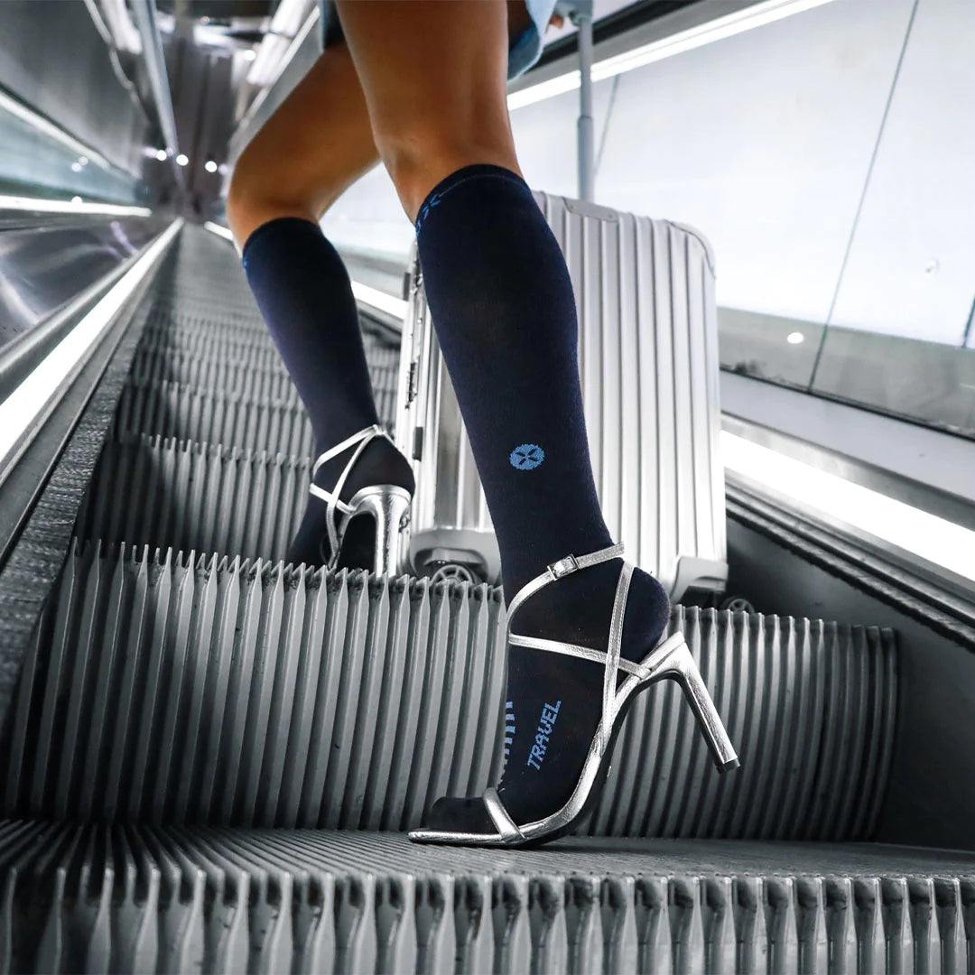 Woman walking on an escalator wearing navy knee high socks and silver heels. 