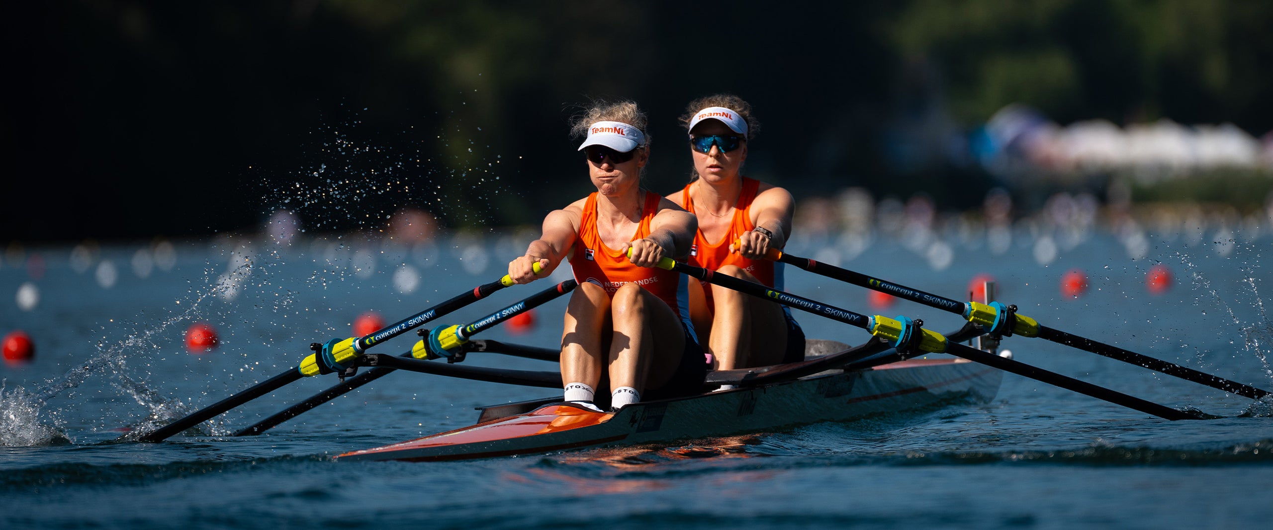 Two women in a rowing boat wearing orange tanktops. 