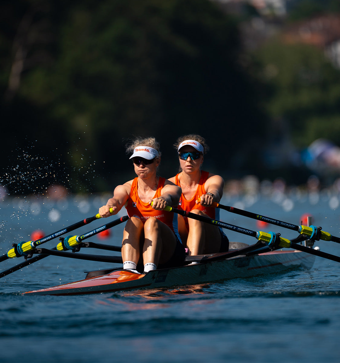 Two women in a rowing boat wearing orange tanktops.  - 