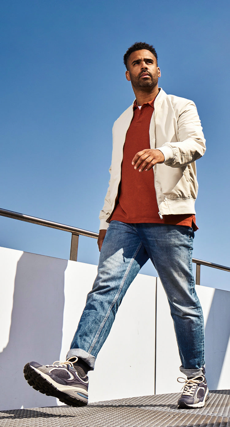 Man wearing jeans walking in the sun with blue sky behind him.