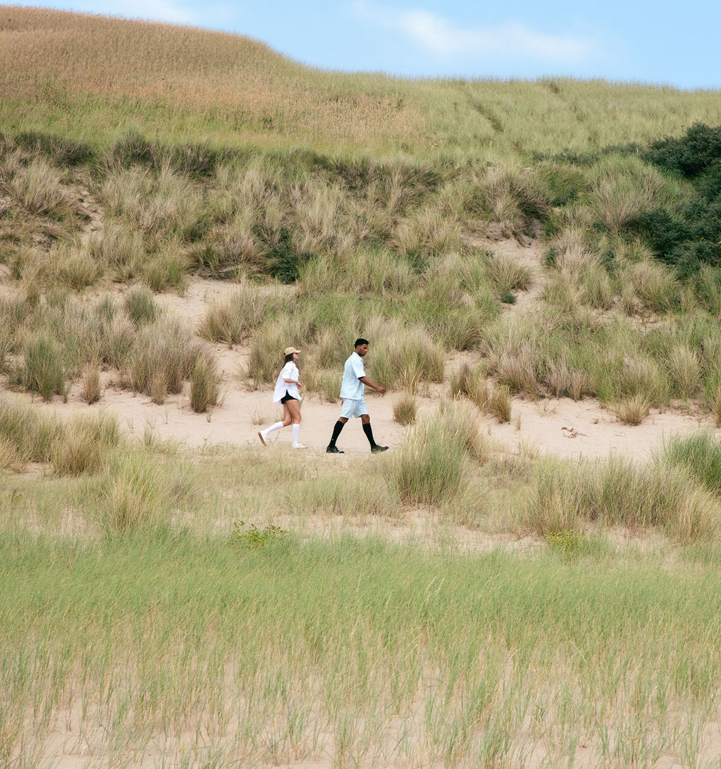 Two people are walking one behind the other in a green environment.