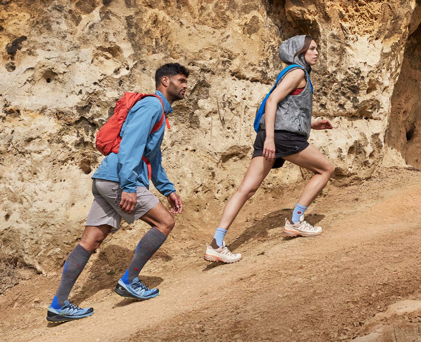 A man and a woman are walking on a rock, both wearing high socks.