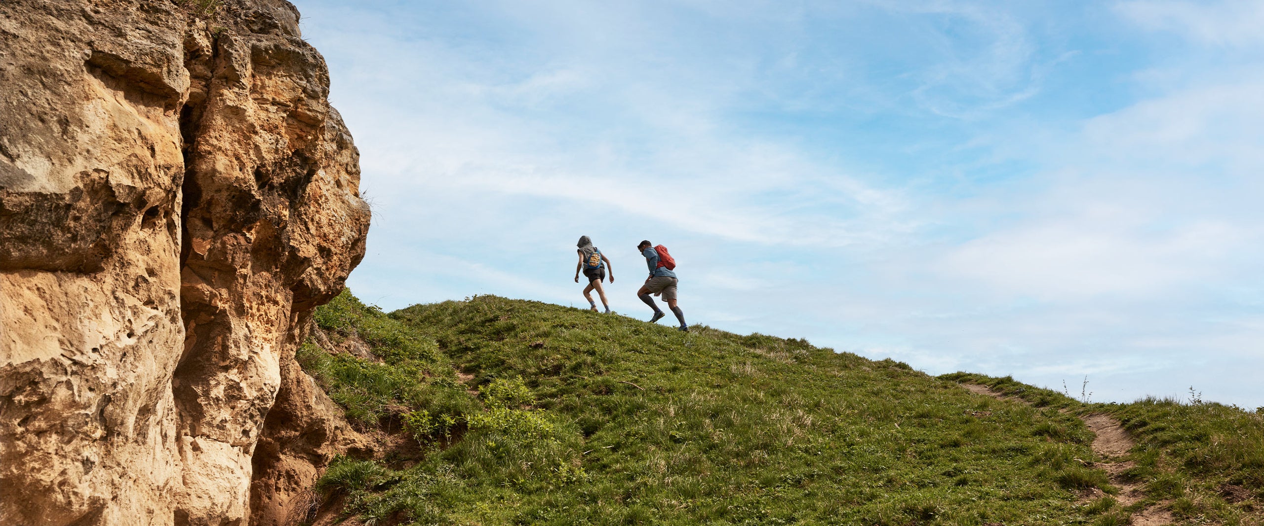Two people walk uphill through a green pasture.
