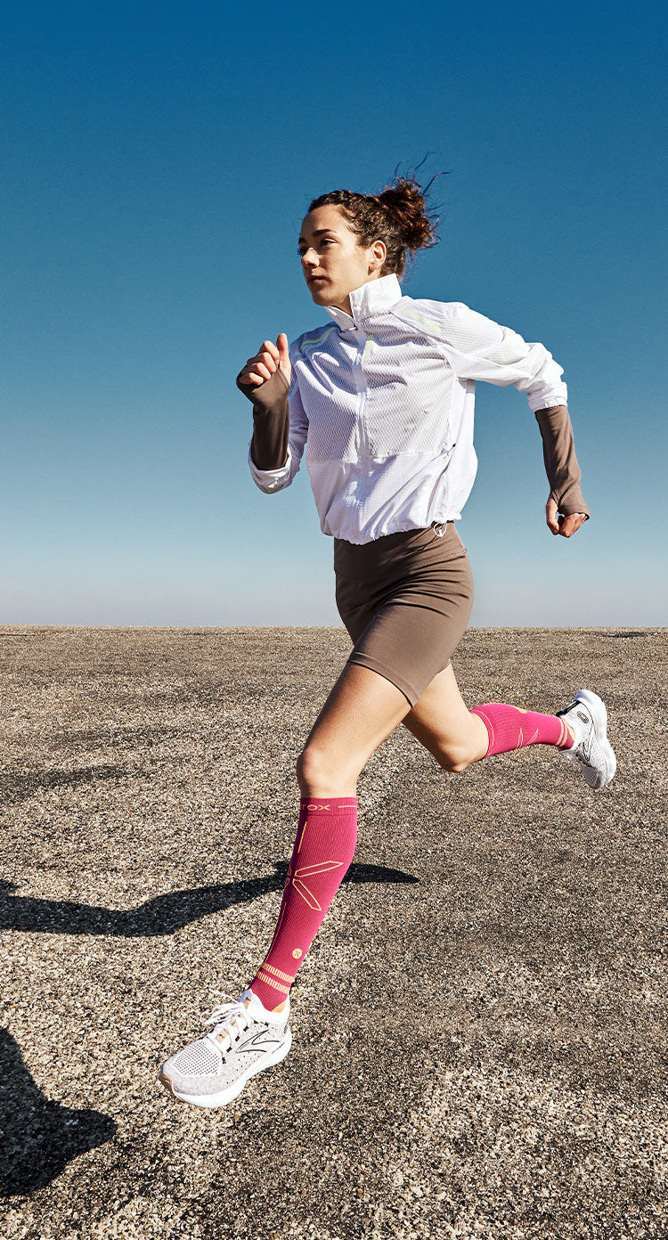 Woman running across concrete field wearing pink socks. 
