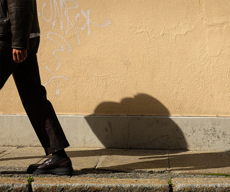 A leg wearing brown pants with a yellow wall in the background.