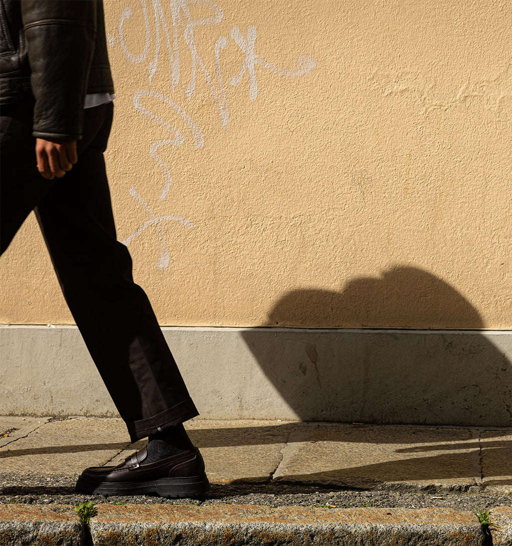 A leg wearing brown pants with a yellow wall in the background.