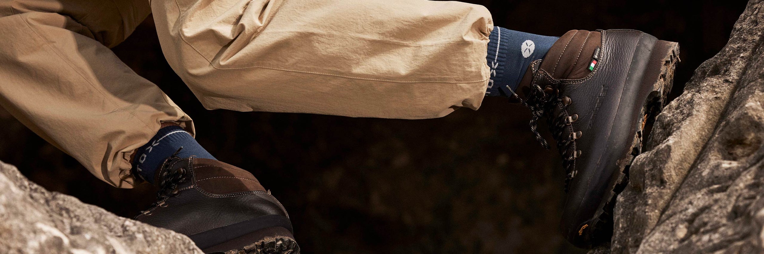 Close-up of a person wearing brown boots with visible soles on a rocky surface.