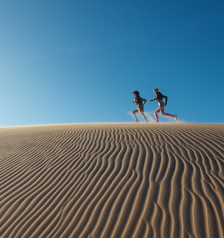 Two people running on a sand dune with a clear blue sky