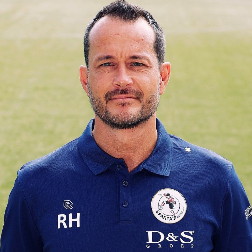 Man standing on grass field wearing dark blue polo with logo's.