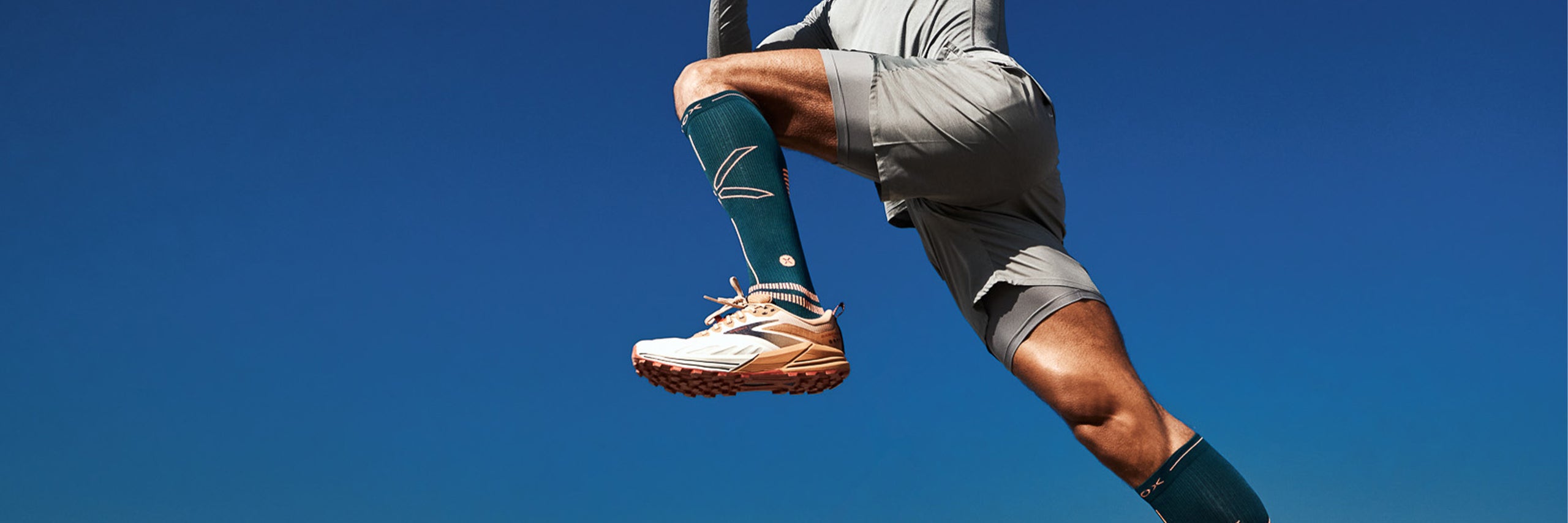 Jumping legs in the blue sky wearing green compression socks. 