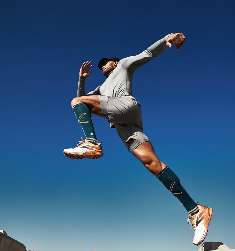 Jumping legs in the blue sky wearing green compression socks. 