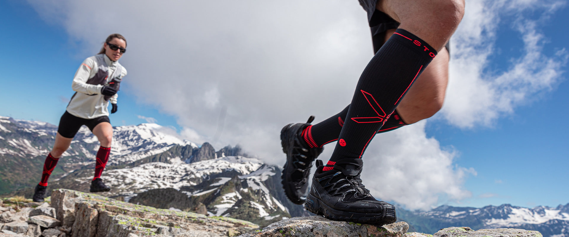 Couple running on rocks in the mountains with high knee socks.