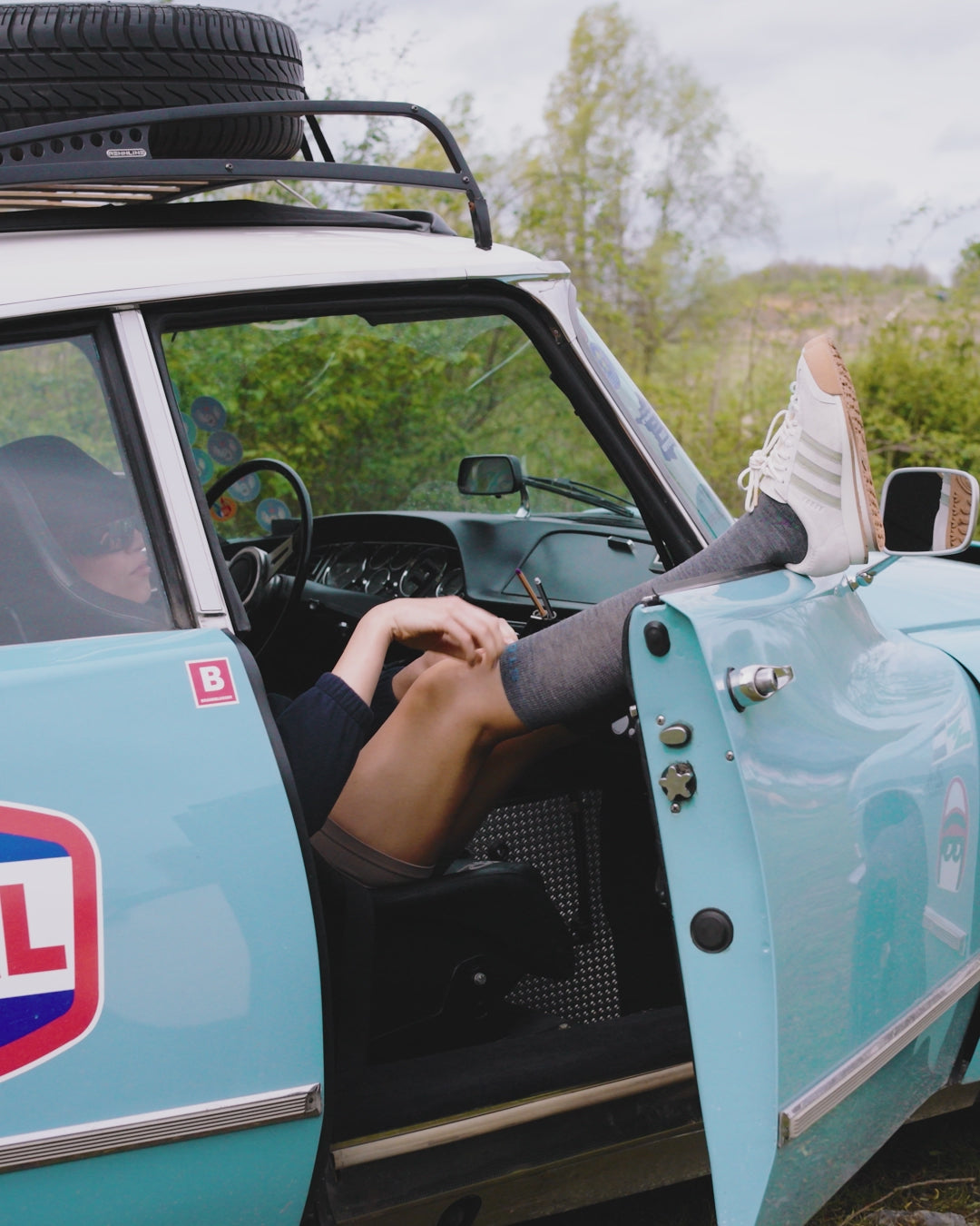 Girl hanging her legs out of a blue old car.