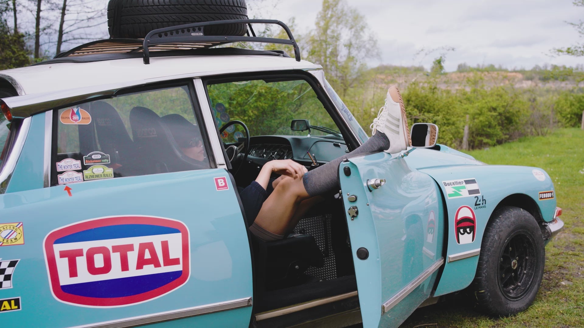 Girl hanging her legs out of a blue old car.
